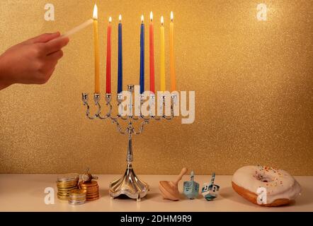 Giorno 7 della festa religiosa ebraica Hanukkah con la mano del bambino illuminazione 7 candela in tradizionale lampadario menorah su luccicanti dorati sfondo wit Foto Stock