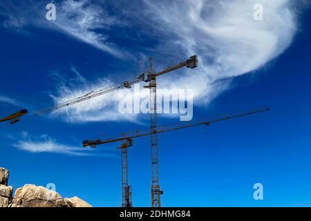 Molte gru a torre alta lavorano per la costruzione di nuove case. Due gru da costruzione contro il cielo blu. Costruzione industriale di buil multi-piano Foto Stock