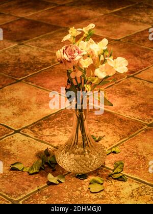 Bella primo piano foto di rose bianche essiccate in bouquet autunno in vaso di vetro trasparente su rustico pavimento piastrelle vecchie. Foglie essiccate caduto da Foto Stock