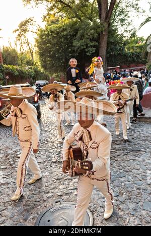 Una tradizionale banda messicana di mariachi suona come marionette giganti chiamate mojigangas danza durante una festa di nozze che pareggia attraverso le strade di San Miguel de Allende, Guanajuato, Messico. Foto Stock