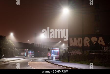 Un passeggero attende alla fermata Cumberland Basin Metrobus durante una nebbiosa notte d'autunno sulla South Bristol Busway. Foto Stock