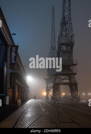 Le vecchie gru portuali sono avvolte nella nebbia all'esterno del museo M Shed in una notte nebbiosa sul porto galleggiante di Bristol. Foto Stock