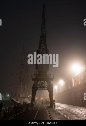 Le vecchie gru portuali sono avvolte nella nebbia all'esterno del museo M Shed in una notte nebbiosa sul porto galleggiante di Bristol. Foto Stock