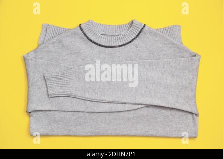 Pullover lavorato a maglia di colore grigio alla moda su sfondo giallo in stile flay lay. Colore del 17-5104 anno 2021 Ultimate Grey e 13-0647 illuminante. Foto Stock