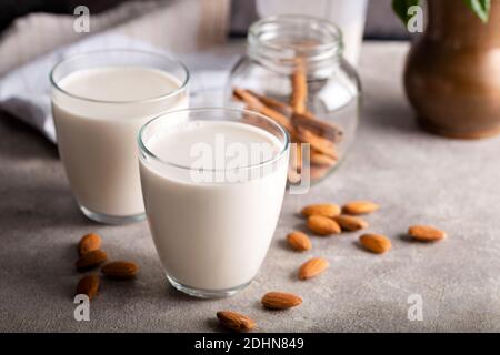 Latte di mandorle biologico fatto in casa in un bicchiere su fondo di pietra con bastoncini di cannella. Foto Stock