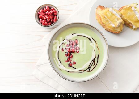 Zuppa festosa di mela verde e piselli con semi di melograno e crostini di camembert cotti in una ciotola su un tavolo di legno bianco, spazio copia, vie ad alto angolo Foto Stock