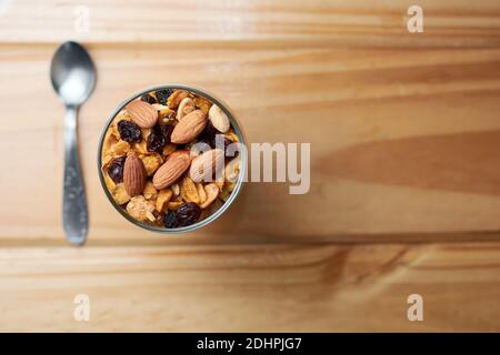 Tazza di muesli e yogurt con uvetta, mandorle e arachidi su tavola di legno che mostra il concetto di cibo gustoso e sano. Vista dall'alto con spazio per la copia. Foto Stock