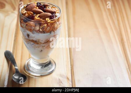 Tazza di muesli e yogurt con uvetta, mandorle e arachidi su tavola di legno che mostra il concetto di cibo gustoso e sano. Spazio di copia. Foto Stock