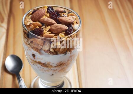 Tazza di muesli e yogurt con uvetta, mandorle e arachidi su tavola di legno che mostra il concetto di cibo gustoso e sano. Primo piano con spazio per la copia. Foto Stock