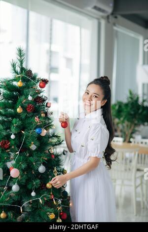 Una giovane donna felice è felice con un albero di Natale splendidamente decorato. Preparazione per Natale. Anticipazione della vacanza. Foto Stock