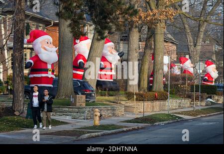 Toronto, Canada. 11 Dicembre 2020. La gente cammina oltre le clausole gonfiabili giganti di Santa su Inglewood Drive a Toronto, Canada, 11 dicembre 2020. A partire dal 2013, decine di clausole di Santa gonfiabili alte 14 piedi si estendono lungo Inglewood Drive a Toronto durante la stagione delle vacanze, attirando molti visitatori. Credit: Zou Zheng/Xinhua/Alamy Live News Foto Stock