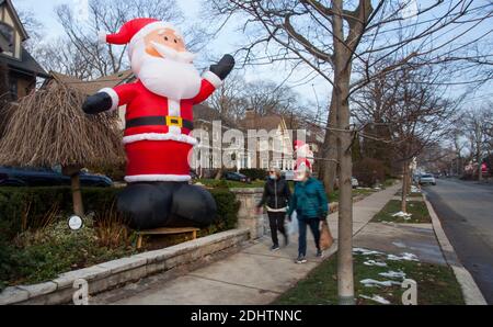 Toronto, Canada. 11 Dicembre 2020. Le persone che indossano maschere facciali camminano oltre un gigante-formato gonfiabile Babbo Natale su Inglewood Drive a Toronto, Canada, 11 dicembre 2020. A partire dal 2013, decine di clausole di Santa gonfiabili alte 14 piedi si estendono lungo Inglewood Drive a Toronto durante la stagione delle vacanze, attirando molti visitatori. Credit: Zou Zheng/Xinhua/Alamy Live News Foto Stock