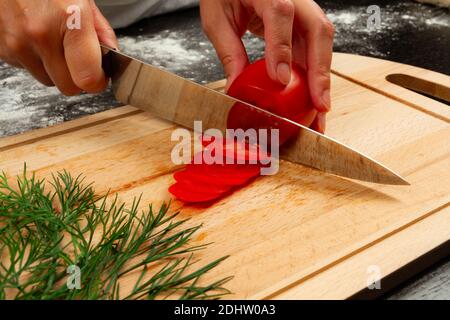 cuoco ragazza taglia pomodori freschi e profumati per preparare la pizza italiana su tavola da cucina in legno Foto Stock