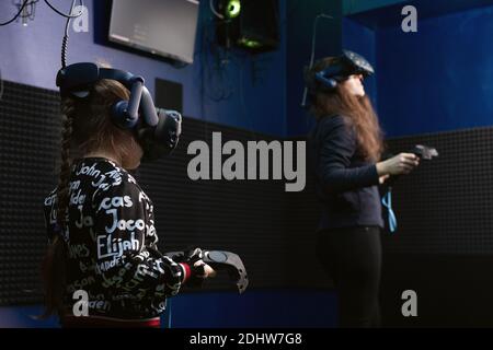 Famiglia che gode della tecnologia VR, figlia e madre nel visore per la realtà virtuale e che gioca ai videogame nel club VR. Tempo libero per la famiglia moderna. Omsk, Russia, Foto Stock