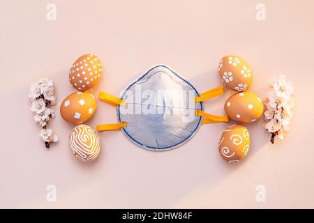 Pasqua in un periodo pandemico. Uova di Pasqua con rami di albicocca fioriti e una maschera protettiva Foto Stock