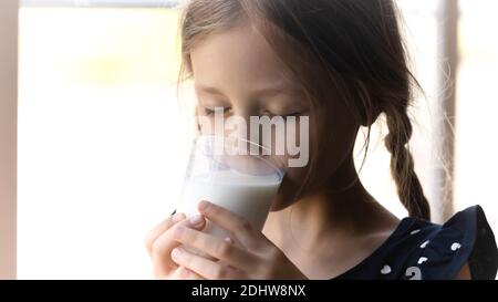 Primo piano cute bambina bere latte, tenendo vetro Foto Stock