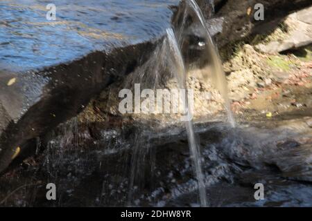 Acqua fresca che scorre su un ruscello di montagna con un tingle di muschio verde che brilla mentre l'acqua fresca cade sopra il bordo in sole parziale e in ombra parziale Foto Stock