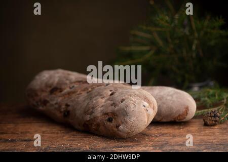 Vörtbröd pane di segale con uvetta su un tavolo di legno. Con rami pinaceae sullo sfondo. Il pane tradizionale svedese di natale ha fatto il pane o il mosto lo Foto Stock