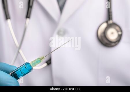 Un medico che tiene una siringa e un ago riempito di liquido blu. Foto Stock