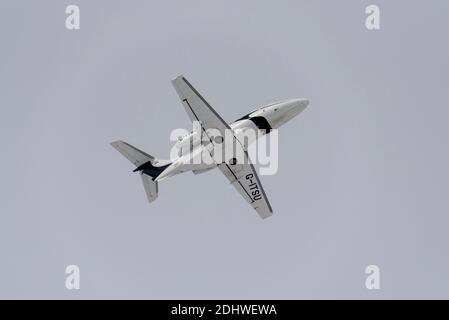 Sovereign Business Jets Embraer EMB 500 Phenom 100 G-ITSU aereo jet aziendale che vola sotto le nubi di neve per unirsi sopra l'aeroporto di Southend a Londra. Lato inferiore Foto Stock