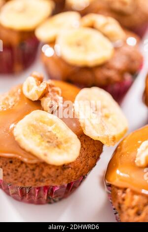 Fresco cucinato banana nut bread muffin spruzzata con fatti in casa caramello, decorate con noci e banana chips. Foto Stock