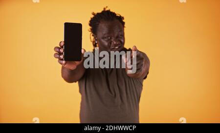 Arrabbiato uomo nero afroamericano che mostra lo schermo del telefono e punta il dito verso la fotocamera. Marito accusato sua moglie. Foto di alta qualità Foto Stock