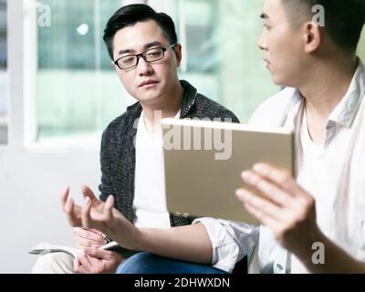 due giovani imprenditori asiatici discutono di business in ufficio utilizzando il digitale tablet Foto Stock