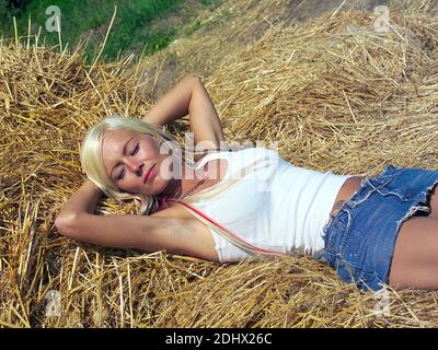 Junge blonde Frau liegt im Stroh, 25,30, Jahre, Urlaub auf dem Bauernhof, Heubetten, MR: Sì Foto Stock