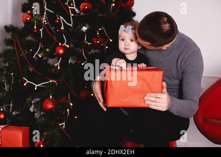 Bambina che disimballa il regalo con papà vicino tree.Happy ragazza disimballa la confezione regalo delle vacanze. Buona famiglia. Foto Stock