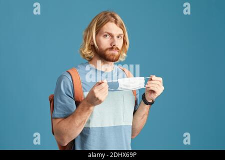 Ritratto di un giovane uomo che indossa una maschera protettiva guardando la macchina fotografica isolato su sfondo blu Foto Stock