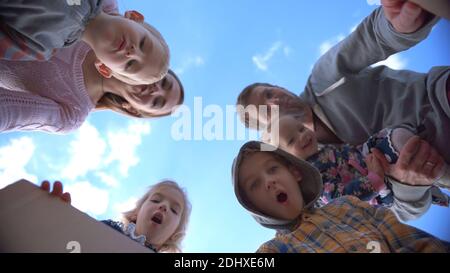 Felice giovane famiglia apre la scatola con regali su uno sfondo di cielo blu. Foto Stock