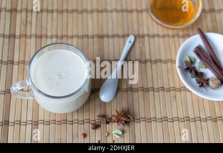 Tè Masala in una tazza di vetro con spezie e miele su sfondo di legno. Bevanda indiana. Orientamento orizzontale. Spazio di copia. Foto Stock