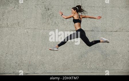 Atleta femminile che corre e salta. Vista laterale dell'atleta flessibile che si esercita all'aperto. Foto Stock