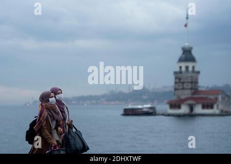 Istanbul, TUR. 12 dicembre 2020. Due donne che indossano maschere protettive e camminano sulla costa di Uskudar con la storica Torre di Maiden sullo sfondo durante un weekend di coprifuoco che è stato imposto per prevenire la diffusione della malattia del coronavirus (COVID-19), a Istanbul, Turchia. Credit: Jason Dean/ZUMA Wire/Alamy Live News Foto Stock