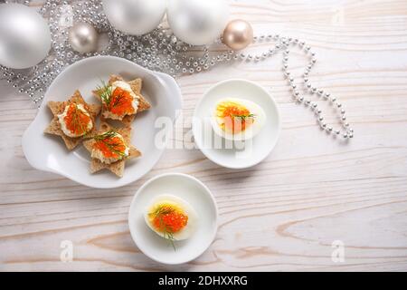 Caviale rosso su uova a metà e su tartine a forma di stella, tavolo in legno bianco con decorazione natalizia per un buffet festivo, spazio copia, angl alto Foto Stock