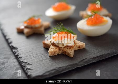 Tartine a forma di stella e uova a metà con caviale rosso e guarnizione aneto su un piatto di ardesia scuro per un buffet festivo di festa, spazio copia, fuoco selezionato, n Foto Stock