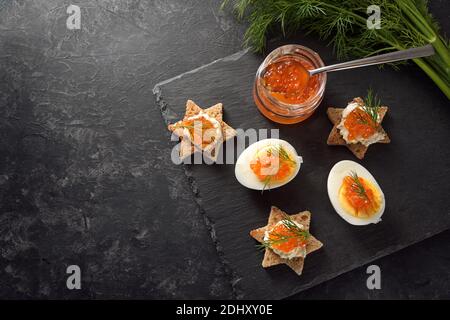 Caviale rosso su uova a metà e su tartine tostate a forma di stella con aneto, preparazione per un buffet natalizio su un piatto di ardesia scuro, copia grande Foto Stock