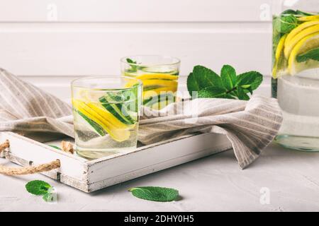 Acqua sassy per detox infuso con limone, cetriolo e menta in bicchieri a bianco vassoio di legno sano concetto di stile di vita. Foto Stock