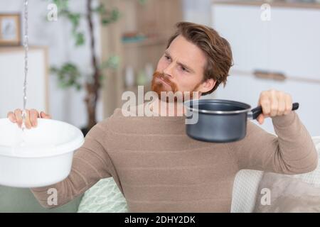 uomo che tiene il bacino di plastica sotto la perdita d'acqua dal soffitto Foto Stock