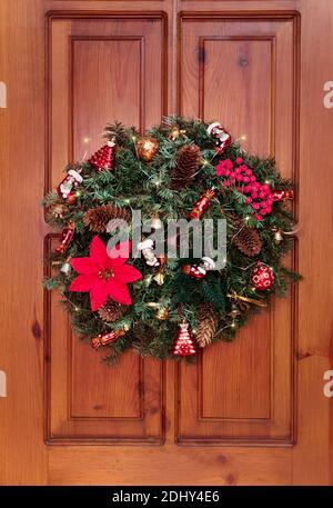 Bella decorazione della porta per Natale e Capodanno. Corona fatta a mano di rami di abete con decorazioni natalizie, stivali, caramelle, bacche, oro Foto Stock