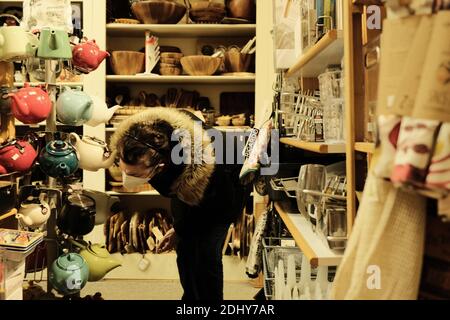 Lo shopper mascherato in una giacca invernale esamina le teiere nel piccolo negozio di cucina a Ottawa, Ontario, Canada. Foto Stock