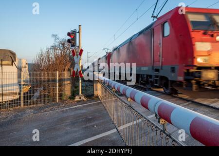 Selective focus view at red and white level crossing railway barrier which block the road and locomotive move on the rail on countryside in winter. Foto Stock