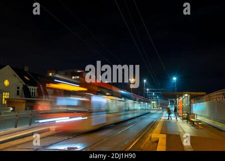 Tram che passa una stazione di notte lasciando un sentiero di luce. Foto Stock