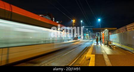 Tram che passa una stazione di notte lasciando un sentiero di luce. Foto Stock