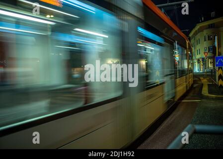 Tram che passa una stazione di notte lasciando un sentiero di luce. Foto Stock