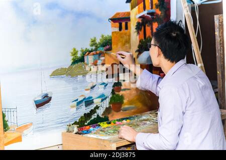 Un artista cinese di pittura ad olio maschile dipinge su una tela nel villaggio di pittura ad olio di Dafen, Shenzhen, provincia di Guangdong, Cina Foto Stock