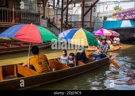 Una donna in una piccola san Pan offre spuntini per la vendita ai turisti in barca più grande con ombrelloni colorati al mercato galleggiante Damneon. Foto Stock