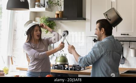 Divertente giovane coppia che finge di combattere con utensili da cucina in cucina moderna Foto Stock