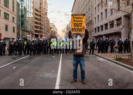 Washington, DC, USA, 12 dicembre 2020. Nella foto: Un manifestante anti-razzismo detiene uno dei segni arancioni della firma del fascismo che dice "Trump/Pence out Now!" Di fronte a una linea di polizia con ufficiali in equipaggiamento antisommossa a Black Lives Matter Plaza questo si è verificato come la polizia ha mantenuto due linee in ogni direzione per mantenere i manifestanti anti anti-razzisti separati dai sostenitori di Trump e dai supremacisti bianchi. Gli ultimi due gruppi sono venuti in città per il milione DI MAGA marzo II per protestare quello che erroneamente pensano è stato un rigato elezione. Credit: Alison C Bailey/Alamy Live News Foto Stock