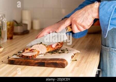 Taglio uomo irriconoscibile con filetto di maiale cotto a coltello grande su tagliere Foto Stock